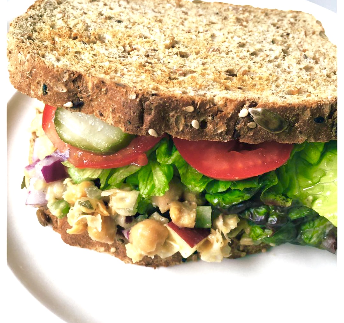 sandwich that looks like tuna but made of chickpeas. Whole grain bread, lettuce, tomatoes, pickles showing