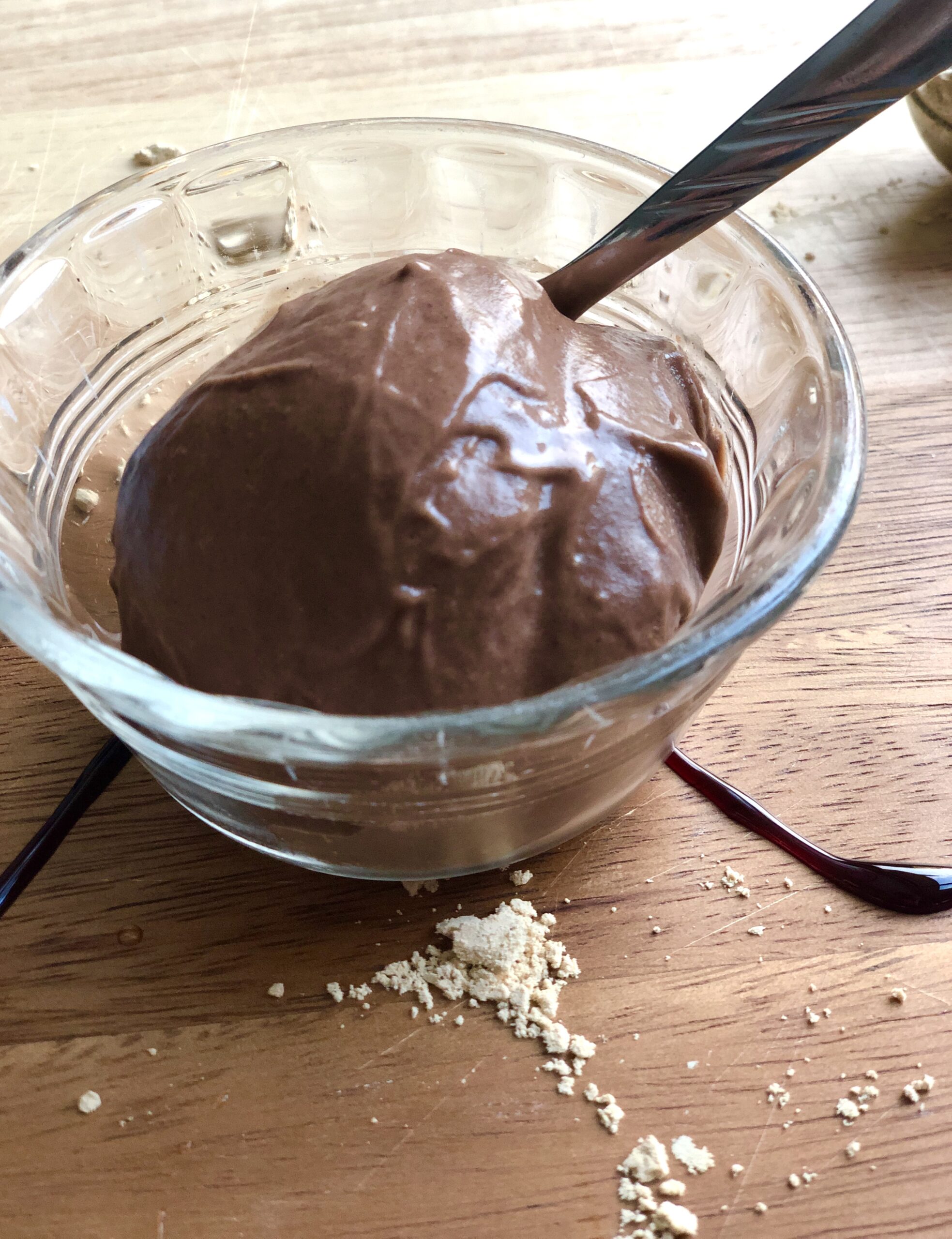 A small bowl of chocolate peanut butter ice cream. There is a spoon in the bowl and peanut butter powder scattered around the bowl.