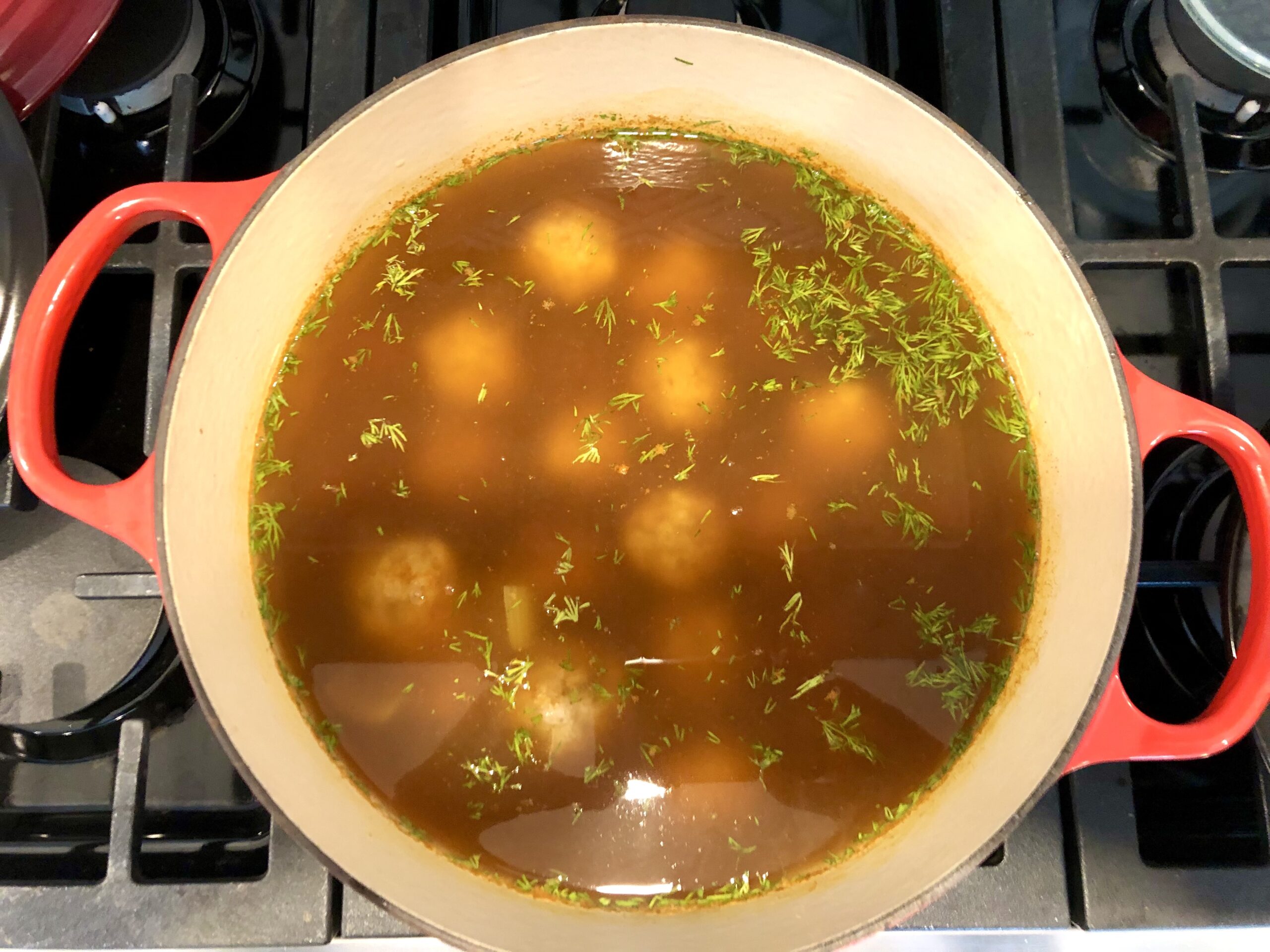 Pot of Matzo Ball soup on the stove. You can see the broth, matzo balls, and some dill