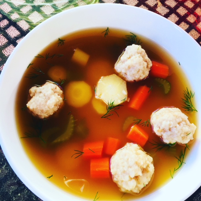 Bowl of matzo ball soup. You can see matzo balls, carrots, celery and dill