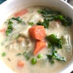 White bowl with a creamy vegetable soup. The broth is white with big chunks of carrots, potatoes, kale, and peas, Creamy Vegetable Soup,